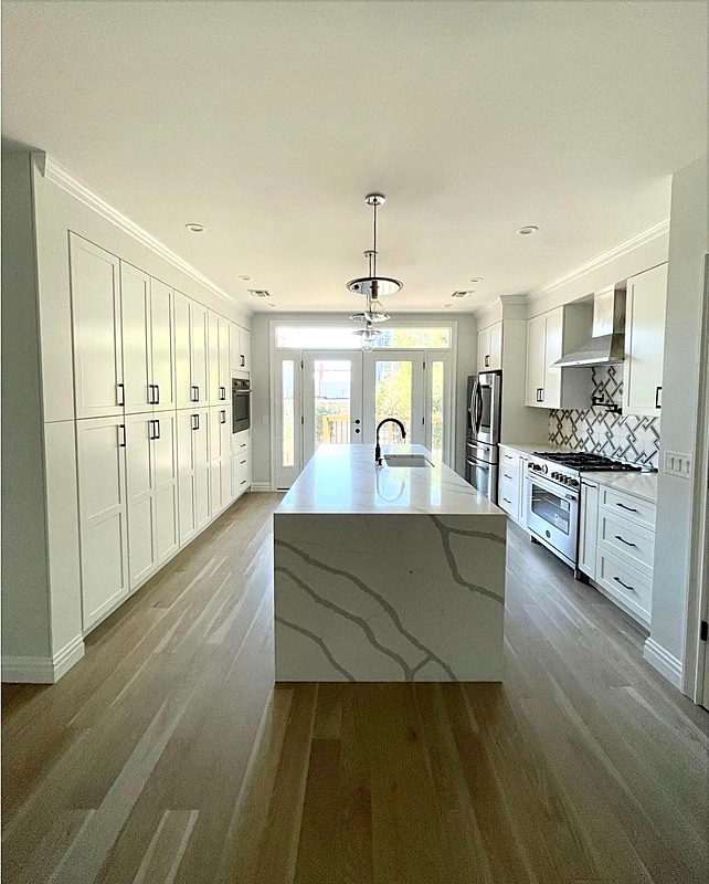 Long white galley kitchen with a quartz waterfall island